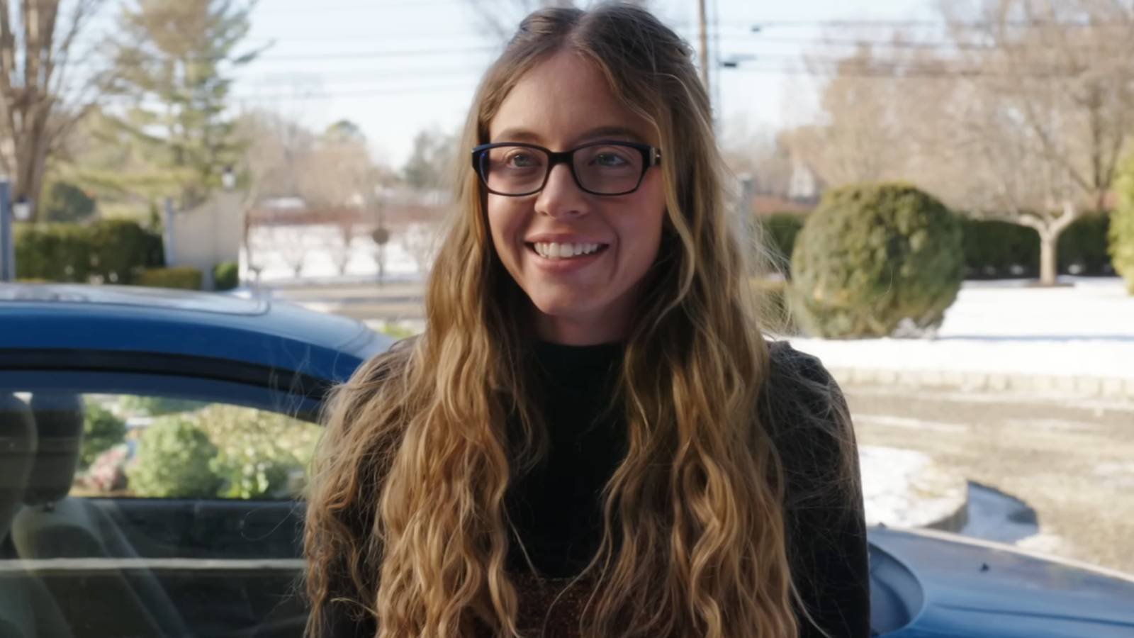 Sydney Sweeney smiling while wearing glasses in The Housemaid