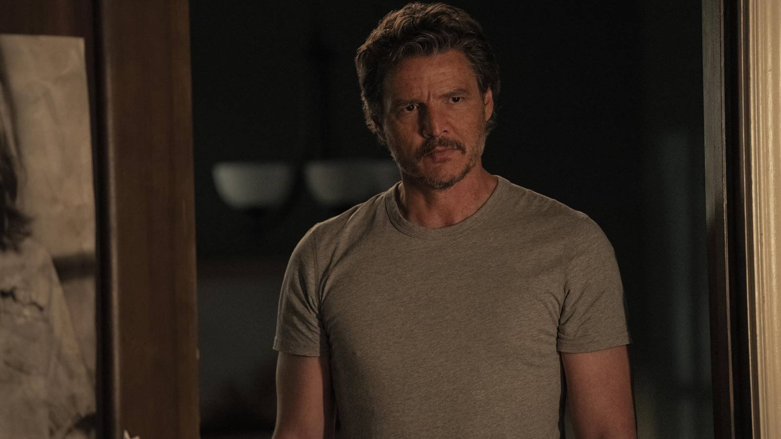 Pedro Pascal as Joel Miller in The Last of Us looking ahead curiously while standing in a doorway