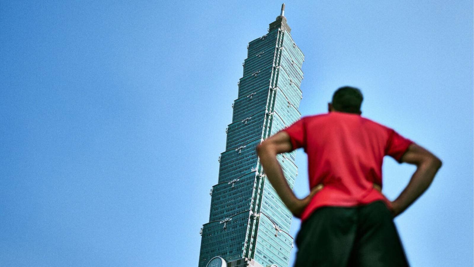 Alex Honnold in front of and looking up at Taipei 101