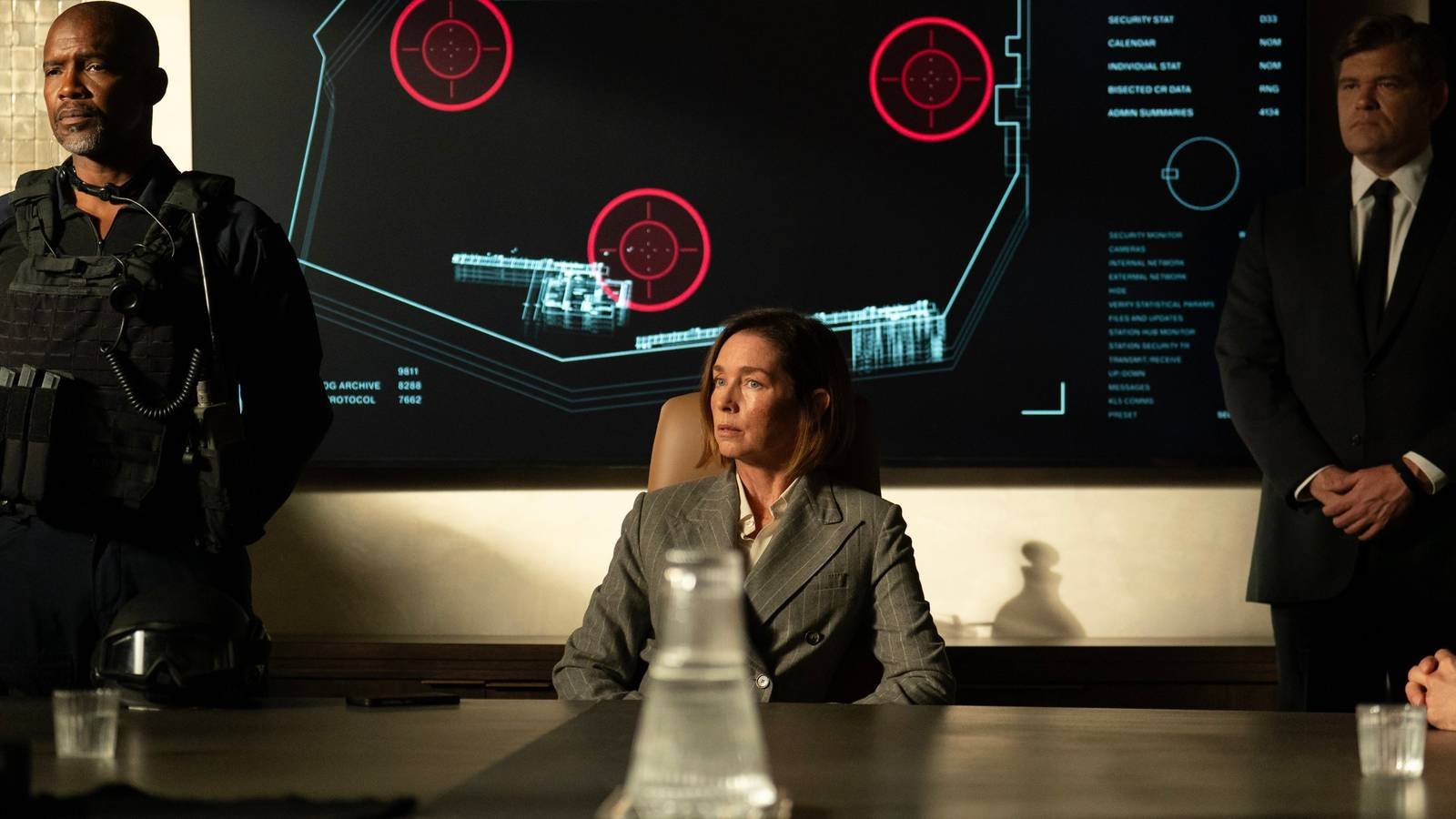 Sinatra (Julianne Nicholson) sitting in the conference room with two security guards either side ...