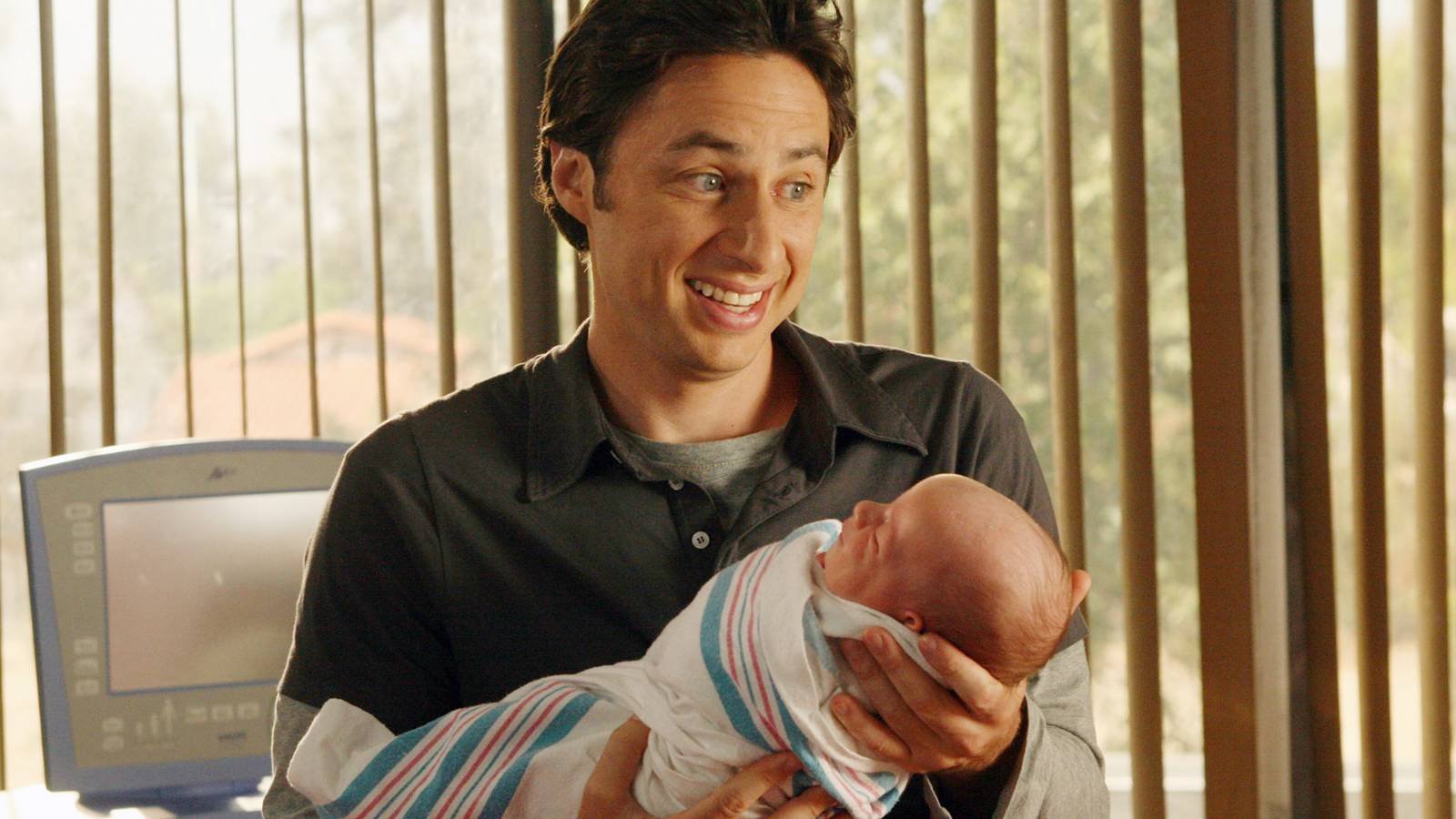 Zach Braff as JD smiling while holding a baby in Scrubs