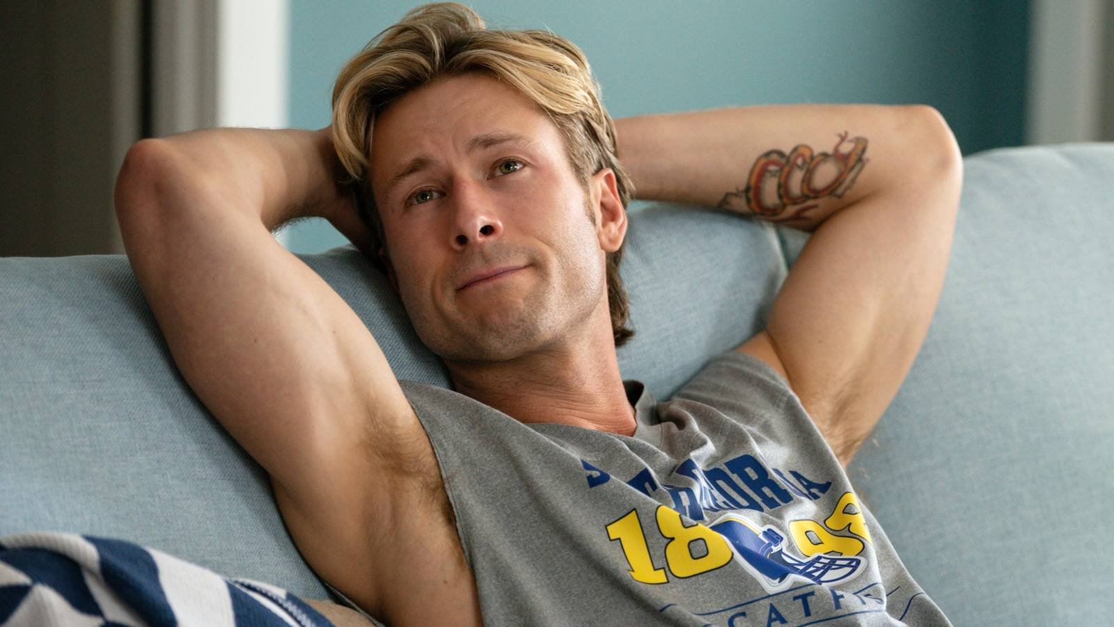Glen Powell showing off his muscles with his arms behind his head in Chad Powers